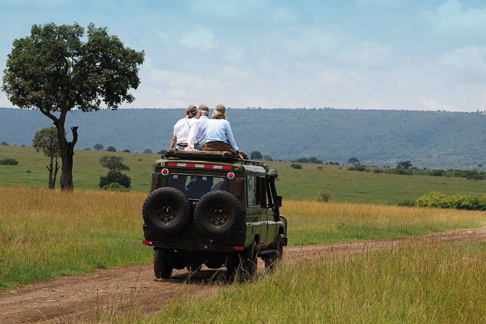 Travelers sit on top of a safari vehicle and look out at Masai Mara National Reserve