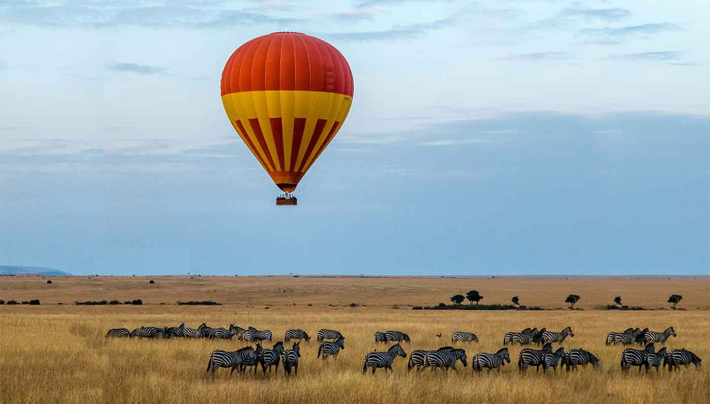 hot air balloon floats above large herd of wildebeest in Kenya