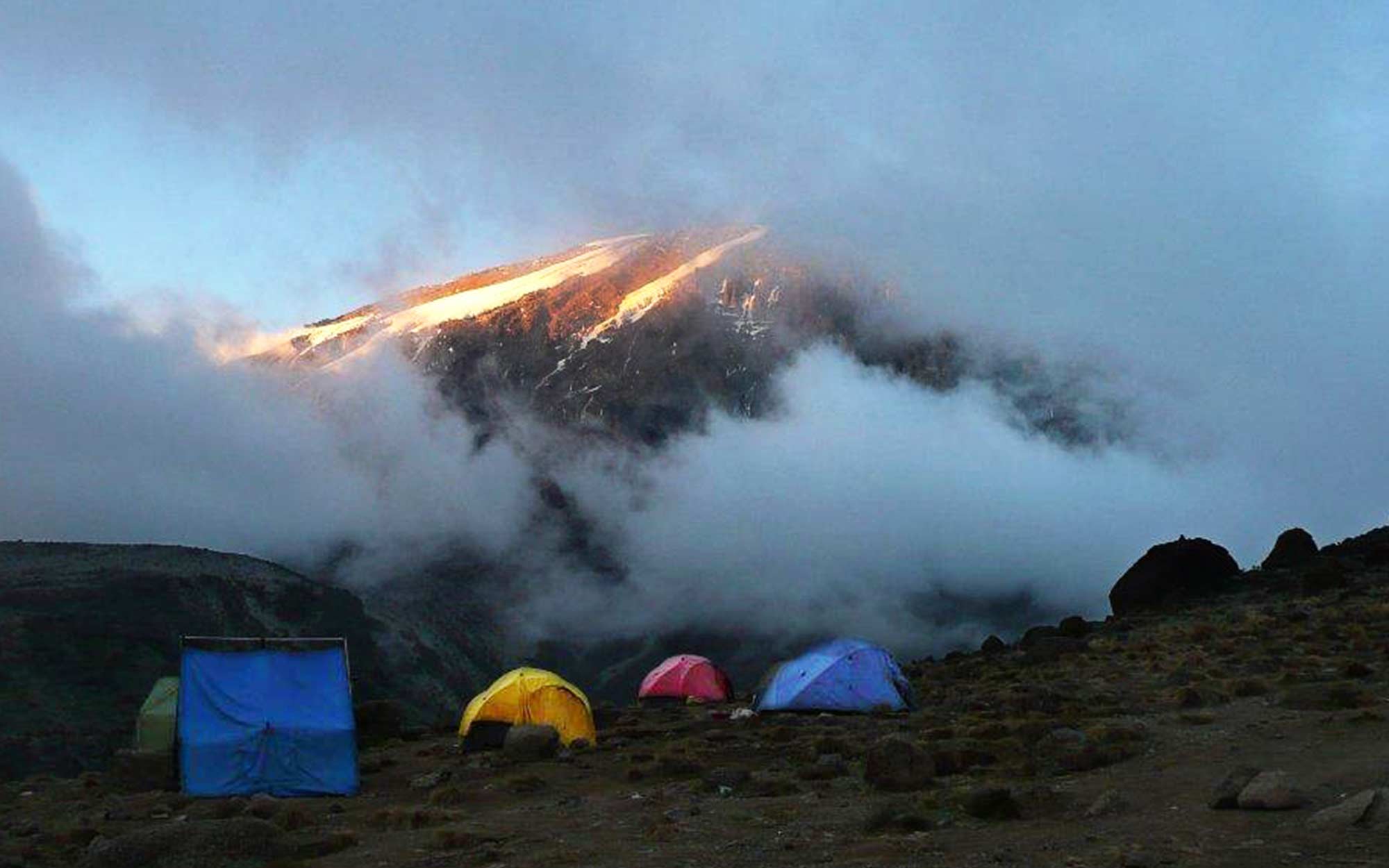 a group of tents are pitched on the ground with Mount Kilimanjaro's peak visible in the background