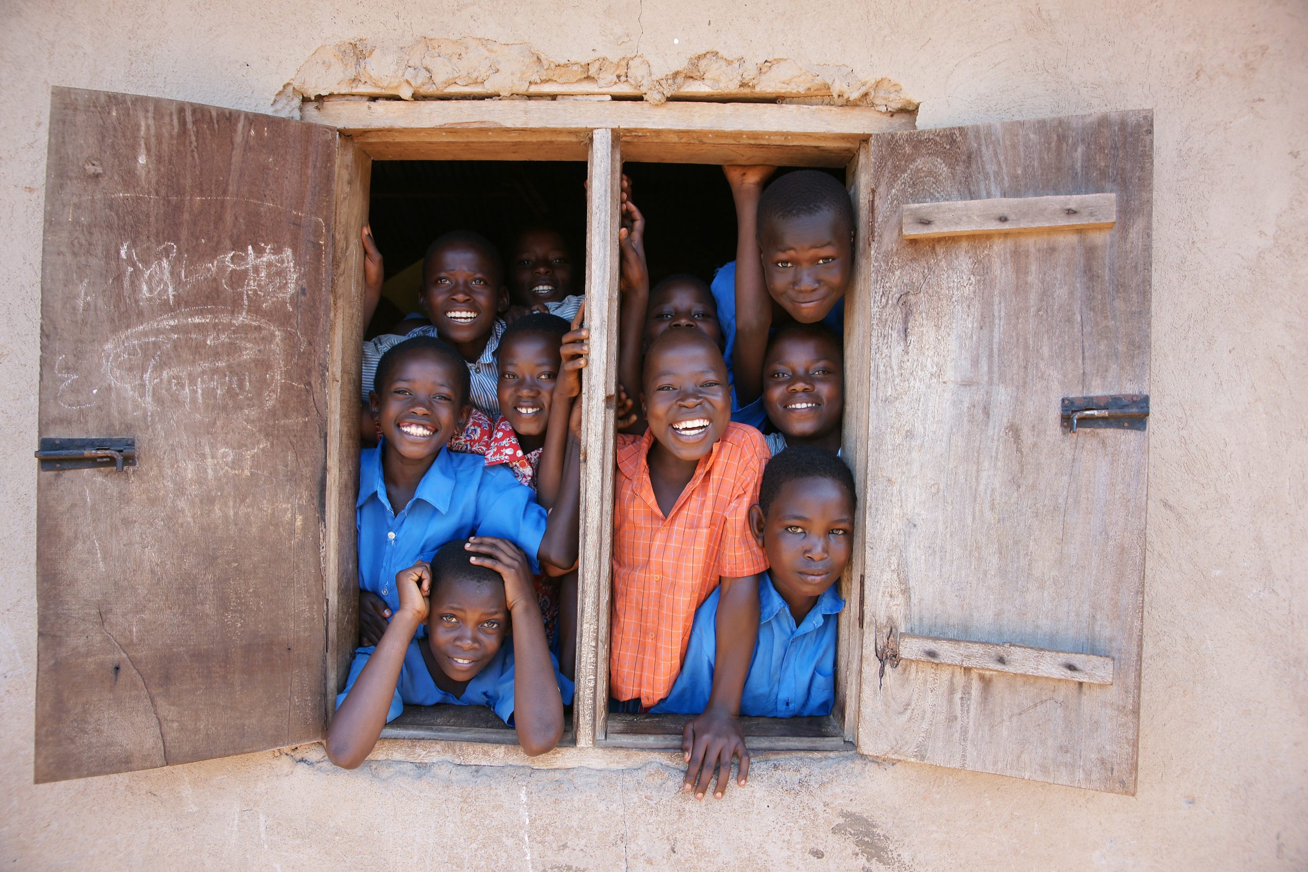 Smiling Ugandan school children gather at classroom window