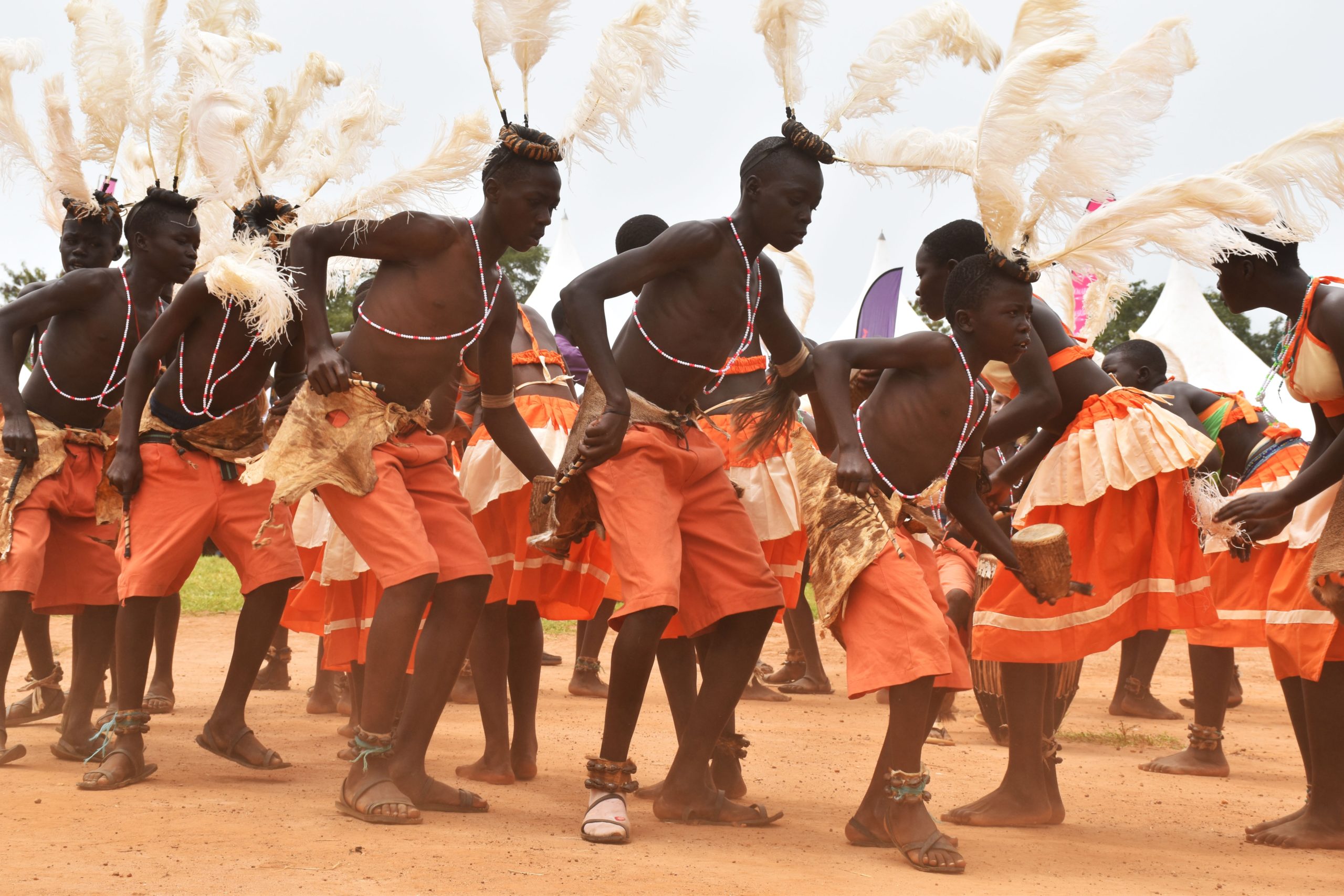 Group of ugandan men in traditional orange clothing perform a traditional dance