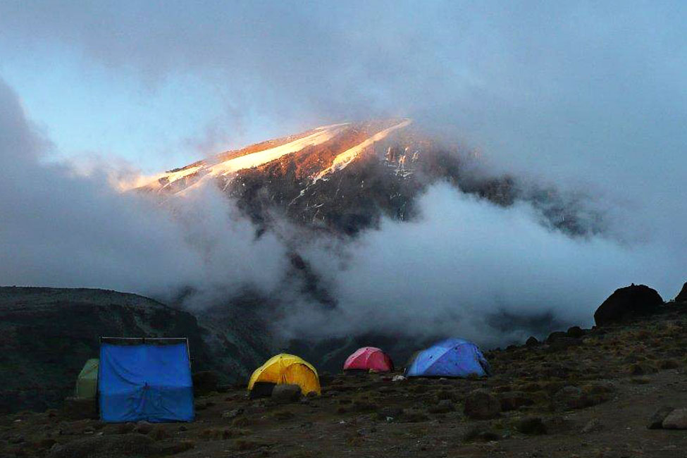 a group of tents are pitched on the ground with Mount Kilimanjaro's peak visible in the background