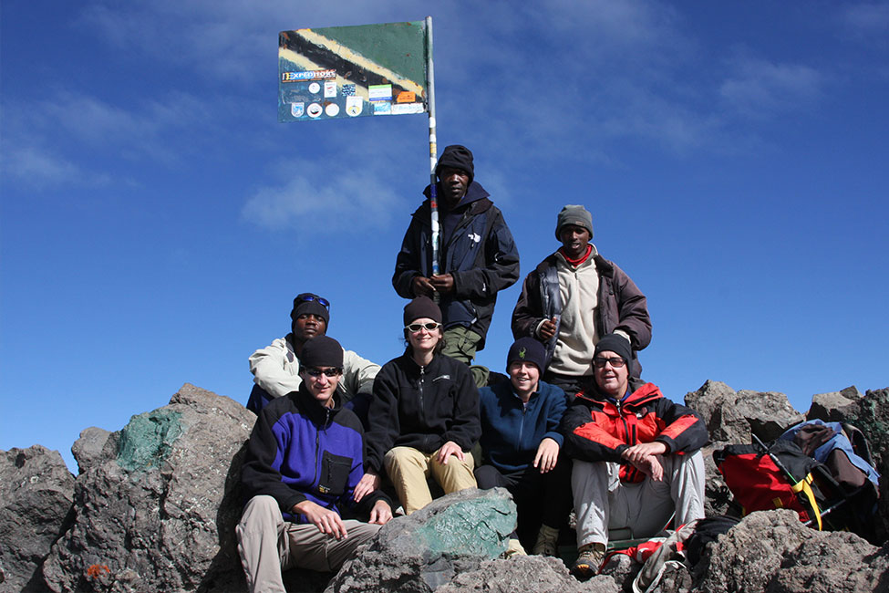 Group of climbers post at the top of Mount Meru with Tanzanian flag