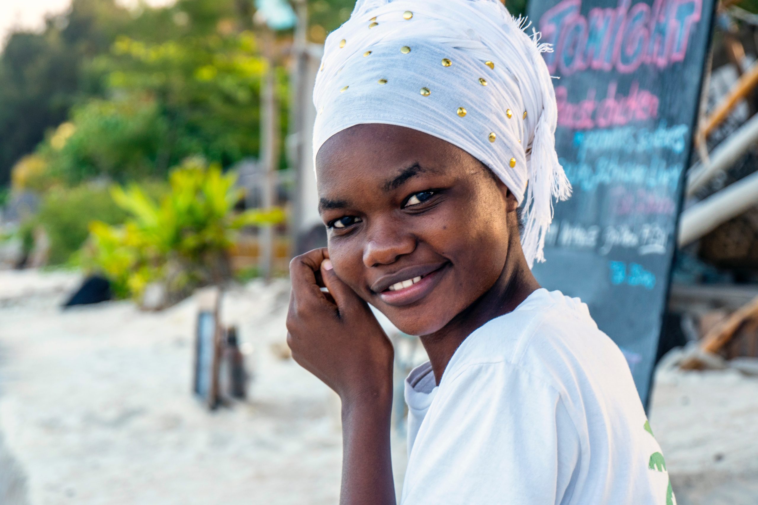 Zanzibar woman in white shirt and white head scarf smiles at camera