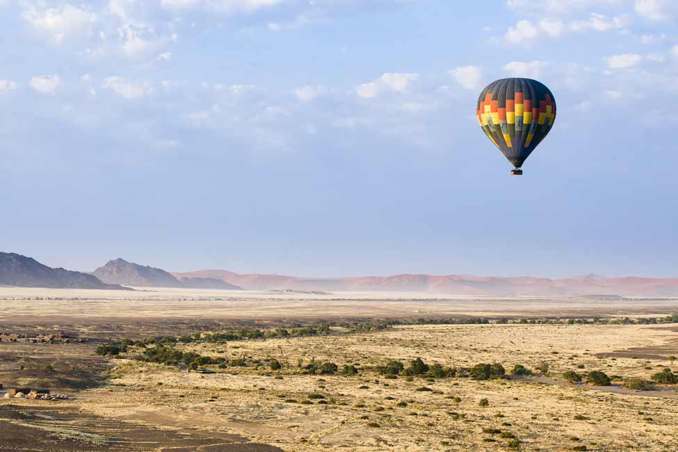 a hot air balloon floats over scrubland in Namibia Africa