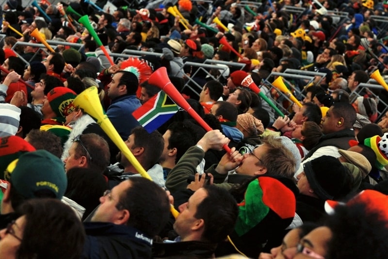 group of spectators in stadium blowing long plastic horns