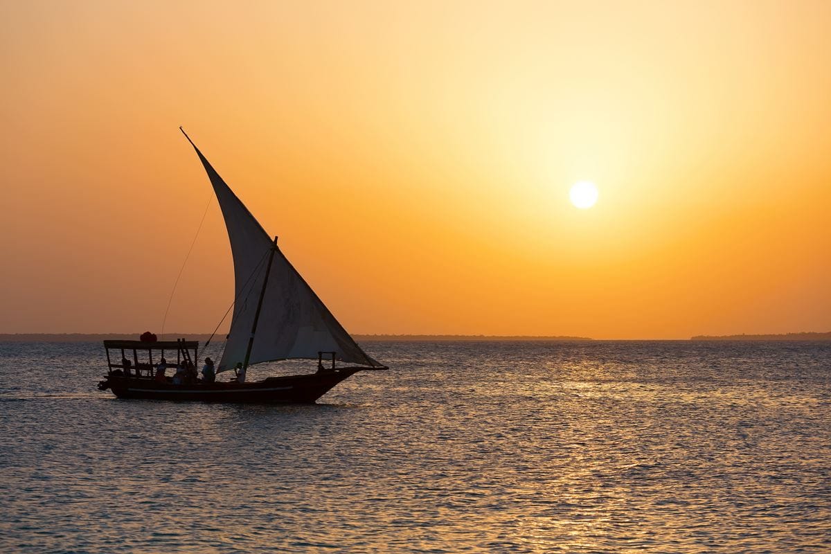 tanzania-zanzibar-sailing-dhow-boat-cruise-shutterstock a dhow sailboat off coast of Zanzibar with sunset in background