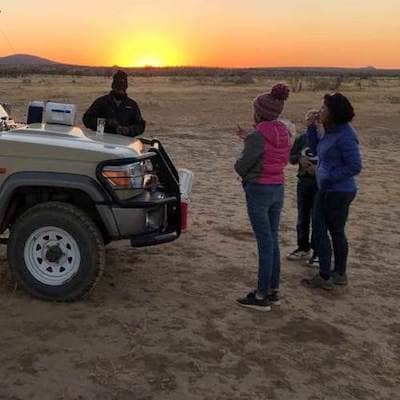 Namibian safari guide and family on safari watch sunset over Namibian desert