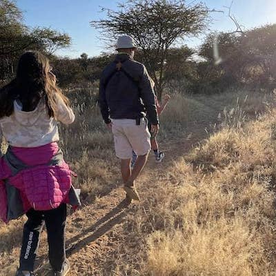 Namibian guide and child traveler walk through short dry grass in Namibian natural area