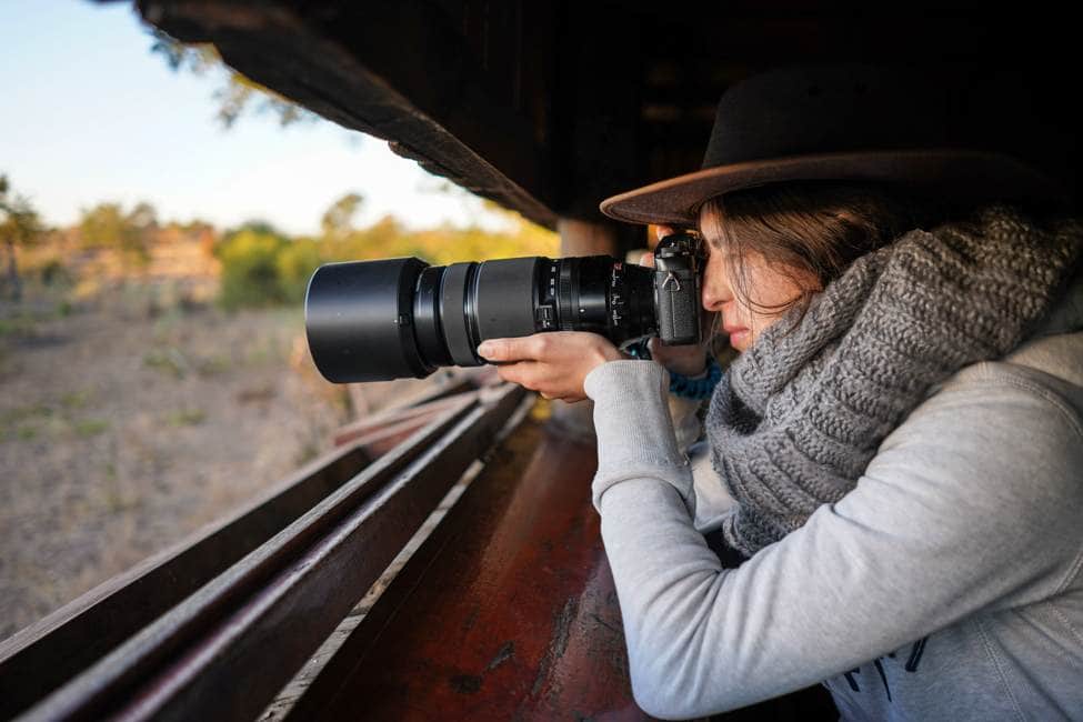 woman with camera and telescoping lens takes photos through the narrow window of a wildlife hide