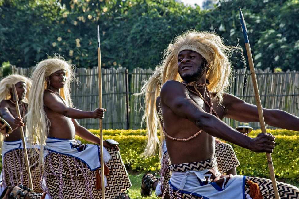 intore dancers in traditional clothing and grass headdresses dance with spears