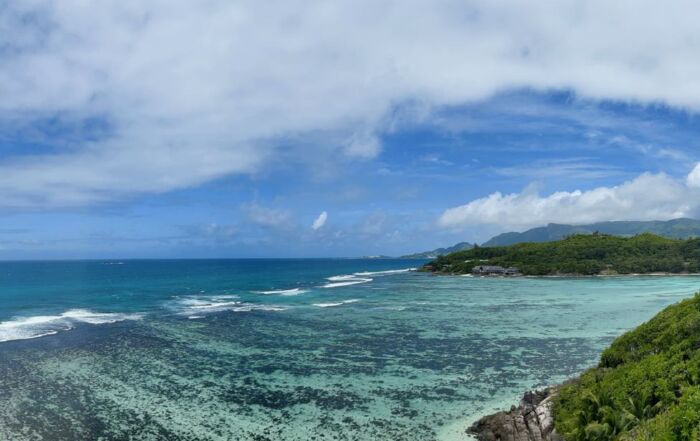 view of Seychelles Moyenne Island coast with shallow blue waters and hilly green forest in background