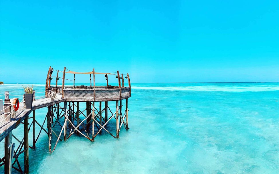 Zanzibar-beach-pier a wooden pier extends out from a beach over turquoise waters in Zanzibar